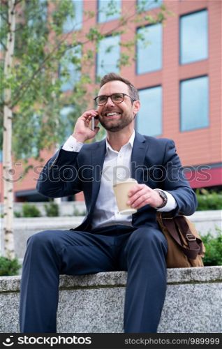 Mature Businessman Taking Phone Call On Mobile Sitting At Outside Office Building