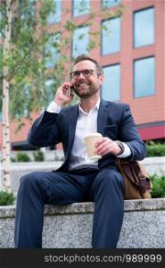 Mature Businessman Taking Phone Call On Mobile Sitting At Outside Office Building