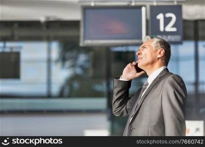 Mature businessman talking on smartphone while standing at boarding in airport