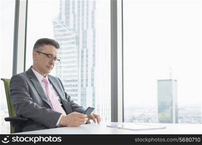 Mature businessman text messaging through cell phone near office window