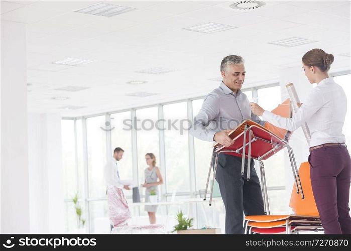 Mature businessman with young businesswoman arranging chairs at new office