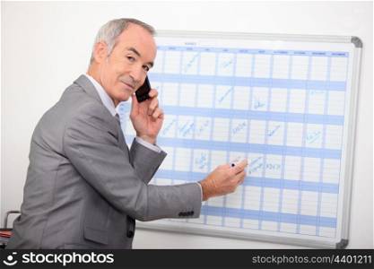 Mature businessman writing on a wall planner
