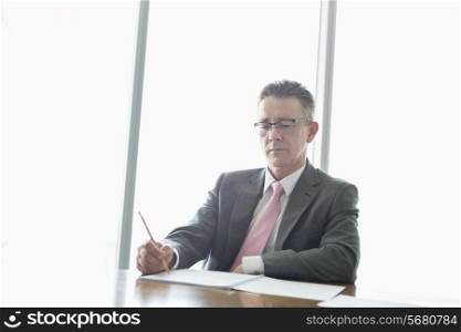 Mature businessman writing on book at table in office