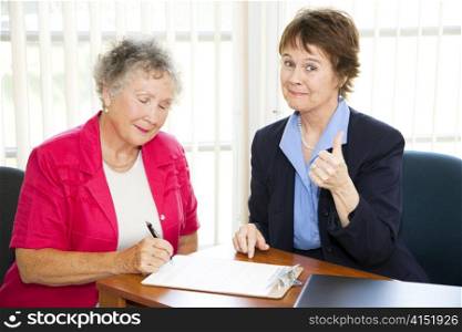 Mature businesswoman gives a thumbs up as her senior client signs sales agreement.