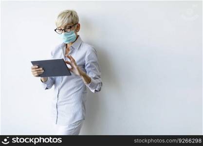 Mature businesswoman using a handheld digital tablet and wear mask to prevent infection by corona virus