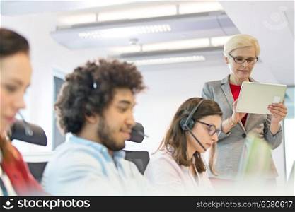 Mature businesswoman using digital tablet while operators working in office