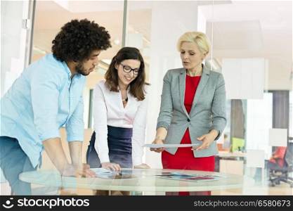 Mature businesswoman with colleagues discussing over project at table in office