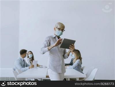 Mature businesswoman with protective mask using digital tablet in the office