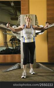 Mature Caucasian adult female using exercise equipment at gym.