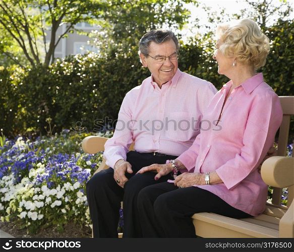 Mature Caucasian couple sitting on bench looking at each other.