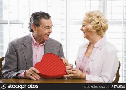 Mature Caucasian man giving Valentine heart box to mature Caucasian woman.