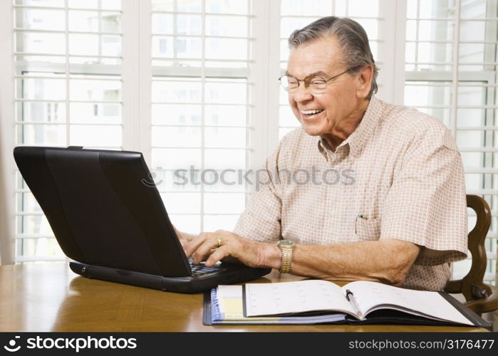 Mature Caucasian man typing on laptop in home.