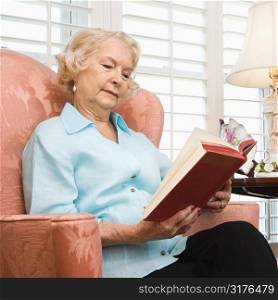 Mature Caucasian woman sitting in chair reading a book.