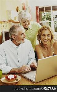 Mature couple and a senior woman smiling in front of a laptop
