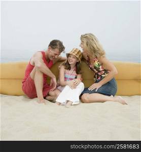 Mature couple and their daughter sitting on the beach with a surfboard