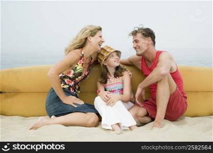 Mature couple and their daughter sitting on the beach with a surfboard