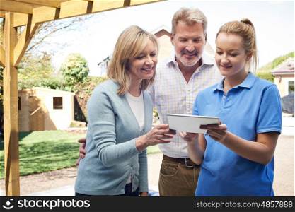 Mature Couple Discussing Plans On Digital Tablet With Landscape Gardener