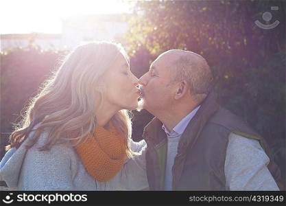 Mature couple face to face kissing in sunlight