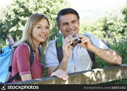 Mature Couple Hiking In Countryside Looking Through Binoculars