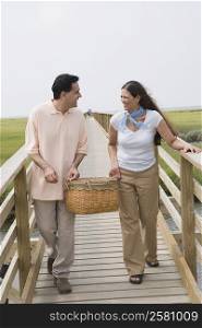 Mature couple holding a basket walking on a footbridge and smiling