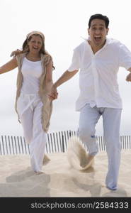 Mature couple holding hands and running on the beach