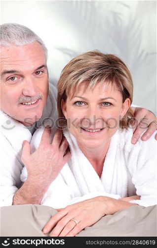 Mature couple in bathrobe laid on a bed