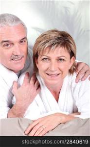 Mature couple in bathrobe laid on a bed