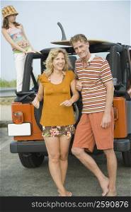 Mature couple leaning against a jeep with their daughter standing behind them