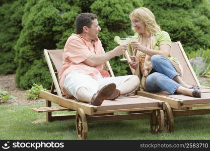 Mature couple leaning on lounge chairs and toasting glasses of margarita