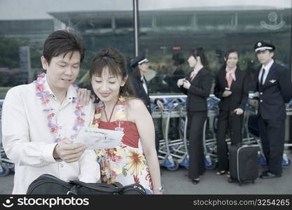 Mature couple looking at an airplane ticket with pilots and cabin crews standing in the background