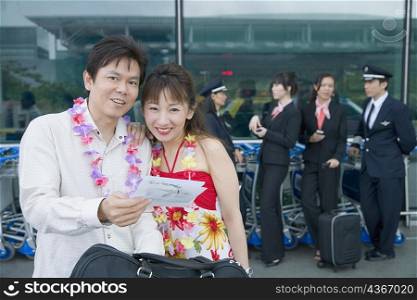 Mature couple looking at an airplane ticket with pilots and cabin crews standing in the background