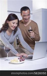 Mature Couple Looking at Laptop in the Kitchen, Drinking Wine