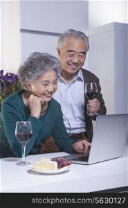 Mature Couple Looking at Laptop in the Kitchen, Drinking Wine