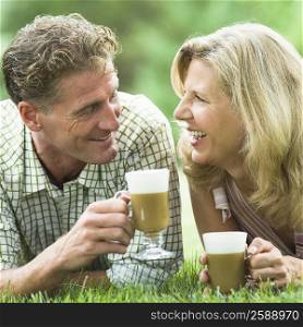 Mature couple lying on grass and drinking iced coffee