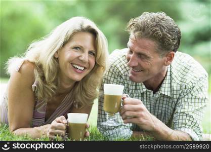 Mature couple lying on grass and drinking iced coffee