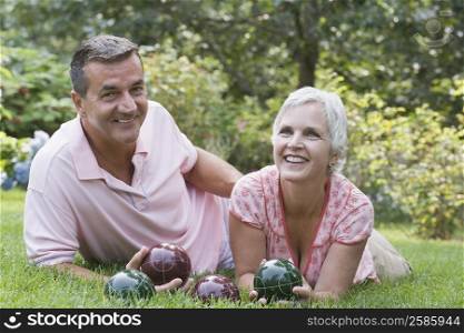 Mature couple lying on grass and holding bocce balls