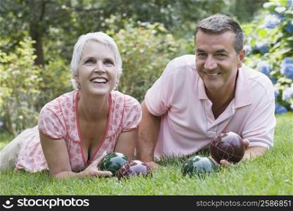 Mature couple lying on grass and holding bocce balls