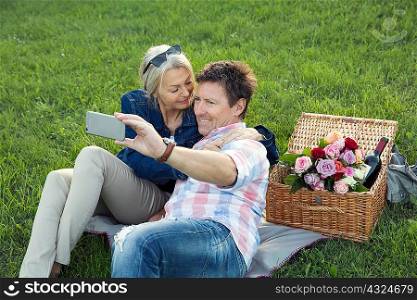 Mature couple on grass having picnic, taking selfie
