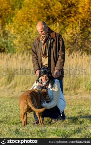 Mature couple playing with retriever dog autumn sunny park