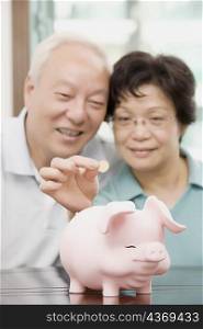 Mature couple putting a coin in a piggy bank