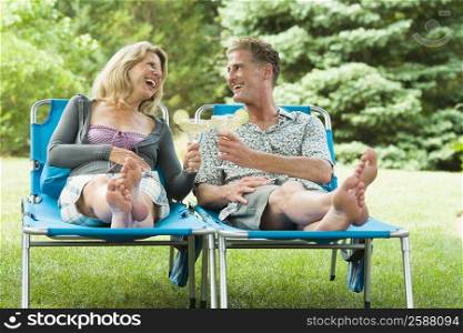 Mature couple reclining on lounge chairs and toasting with glasses of cocktail