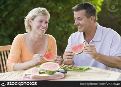 Mature couple sitting at a table and holding slices of watermelon