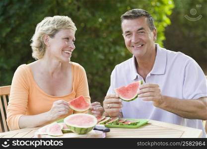 Mature couple sitting at a table and holding slices of watermelon