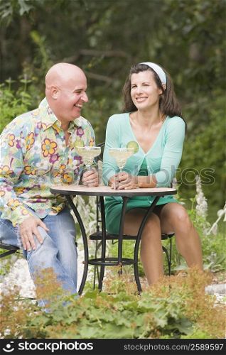 Mature couple sitting at a table holding glasses of margarita