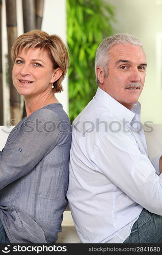 Mature couple sitting back to back at home