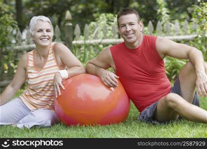 Mature couple sitting in a lawn with a fitness ball and smiling