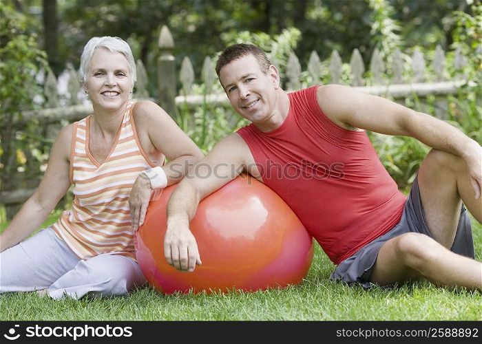 Mature couple sitting in a lawn with a fitness ball and smiling