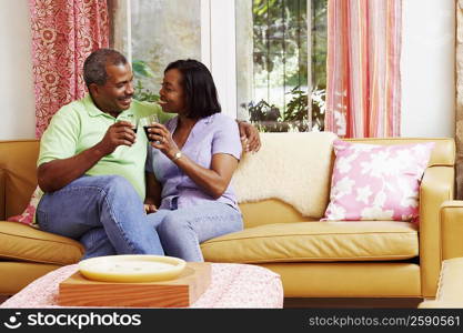 Mature couple sitting on a couch and toasting with glasses