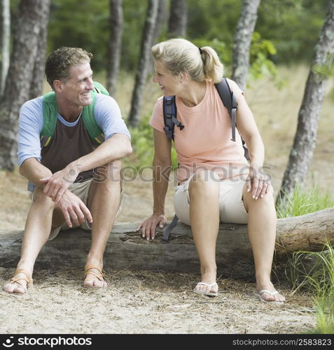 Mature couple sitting on a tree trunk in a forest and looking at each other