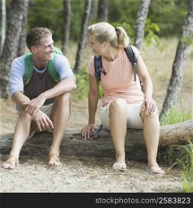 Mature couple sitting on a tree trunk in a forest and looking at each other
